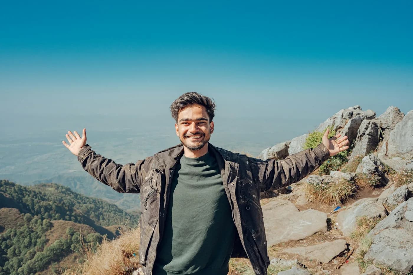 A man smiling with open arms on a mountain top.